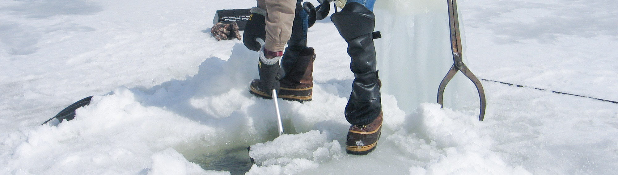 Ice fisherman using the Darkhouse Dipper to remove slush from a fishing hole